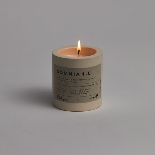Somnia 1.0 Duftkerze von Momo Cotton mit brennender Flamme auf grauem Hintergrund