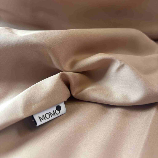 Lençol ajustável bege de bambu dobrado com etiqueta momo-cotton visível, mostrando textura macia