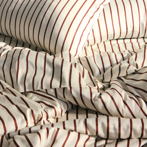 Bamboo duvet cover set with red and beige striped pattern on unmade bed, showing silky texture