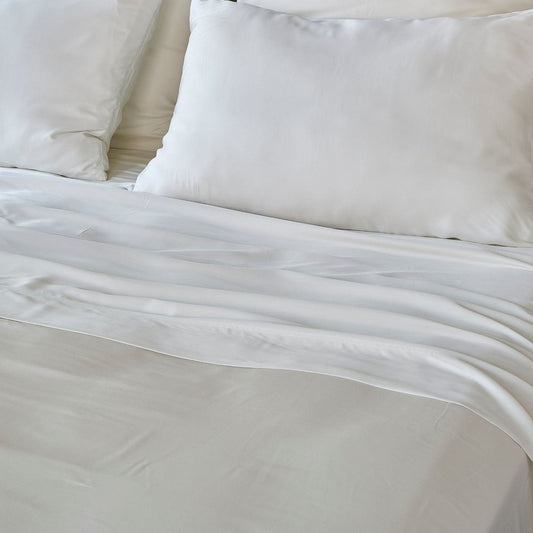 Fronhas de bambu branco exibidas na cama com lençol e almofadas brancas, mostrando textura macia e acabamento liso