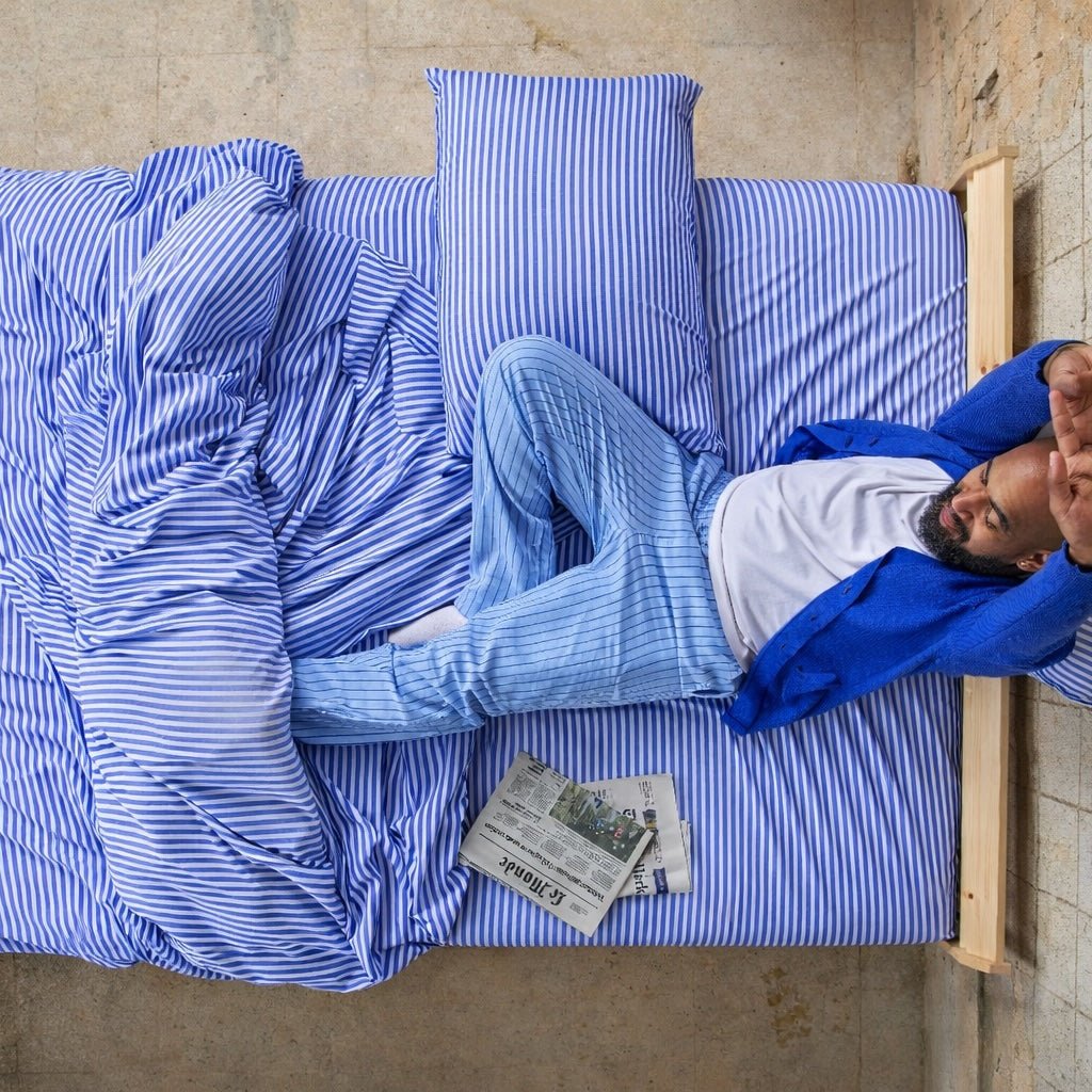 Mann liegt auf Bettbezug mit blau-weißem Muster im Bett mit Zeitung, Draufsicht