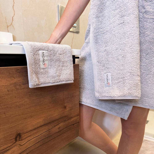 Momo Cotton towel set displayed on wooden bathroom rack with person holding folded beige towels