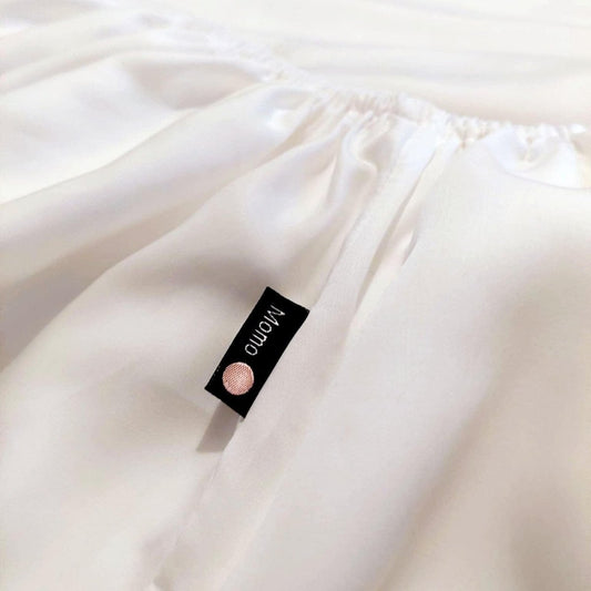 Weißes Bambus-Spannbettlaken mit momo-cotton-Markenlogo auf gefalteter Stoffoberfläche
