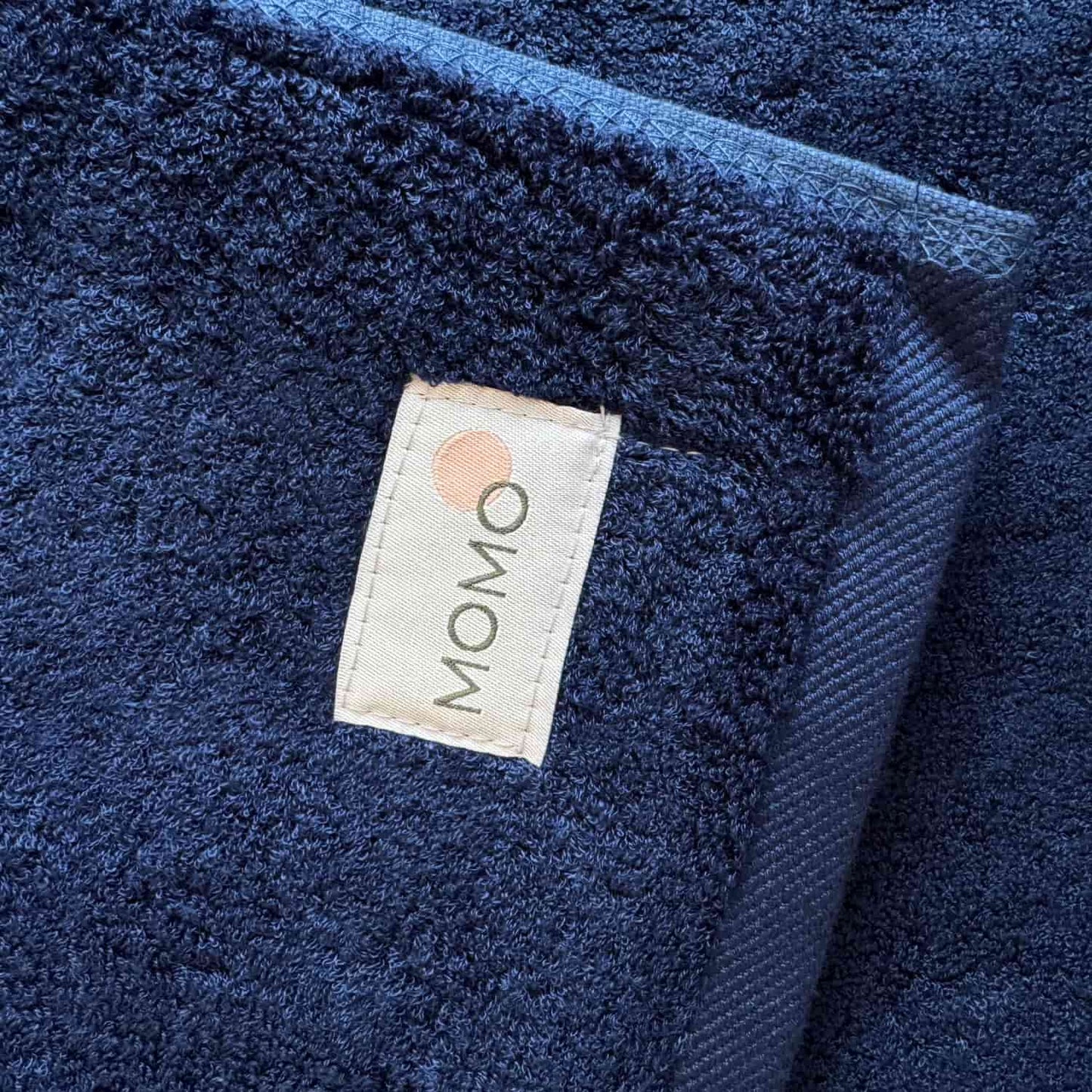 Dunkelblauer Wabi-sabi-Badematte von Momo Cotton mit sichtbarem Markenlogo auf strukturierter Oberfläche
