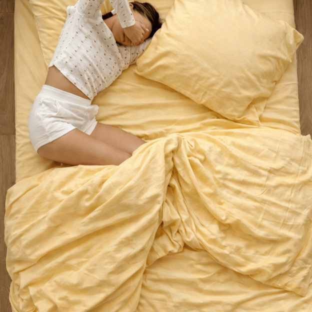 Bett mit gelber Bettwäsche und Kissen, Person in dekorativer Bedscaping-Position liegend.
