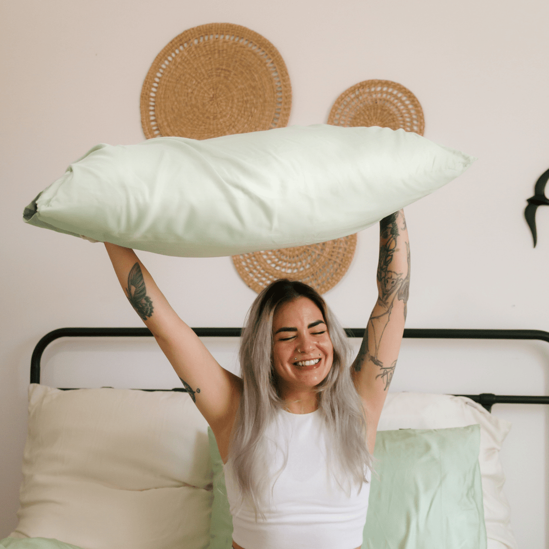 Frau hält weiße, bequeme Bambus-Bettwäsche auf einem Bett
