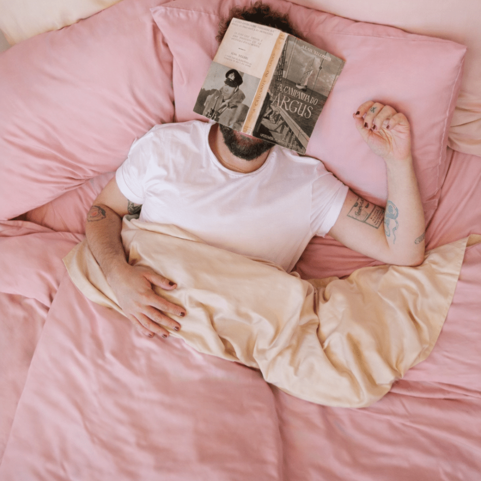 Man lying on pink bamboo sheets in bed while reading a book