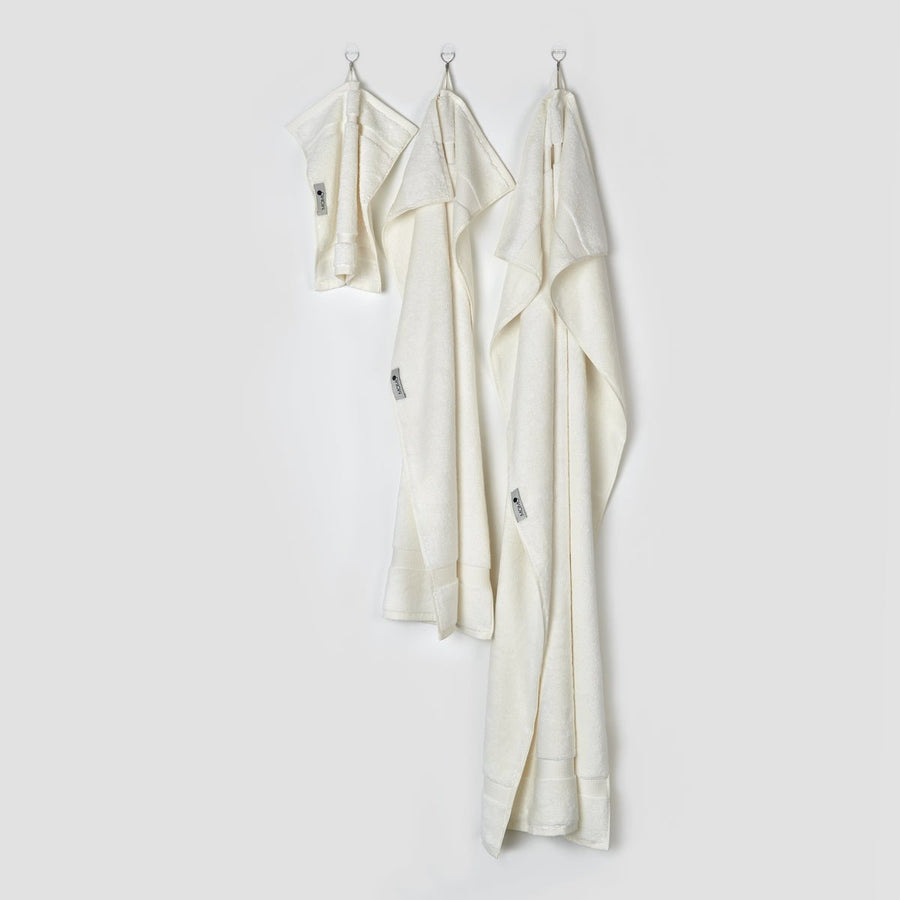 Drei cremefarbene Bambus-Handtücher an Haken in den Größen Gesicht, Hand und Bad aus der Alba-Kollektion von momo-cotton