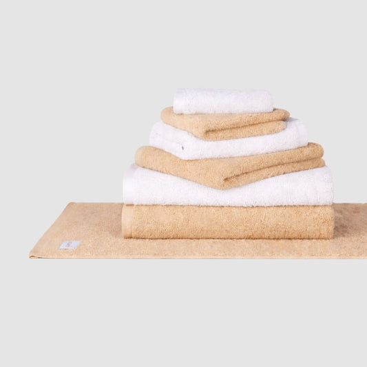 Gestapeltes Handtuch-Set aus Baumwolle in Beige und Weiß von Momo Cotton auf neutralem Hintergrund