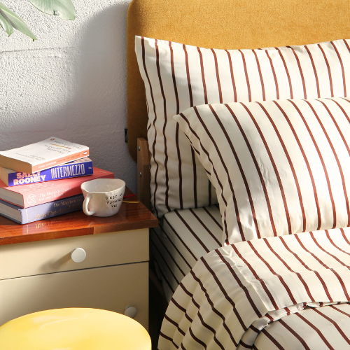 Complete bamboo bedding set with striped pillowcases in neutral tones on wooden bed with nightstand