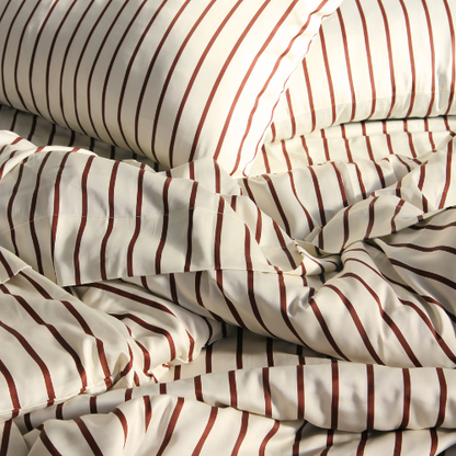Bamboo duvet cover set with red and beige striped pattern on unmade bed, showing silky texture