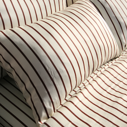 Par de fronhas de bambu acetinado com padrão de riscas bordeaux, dobradas na cama.