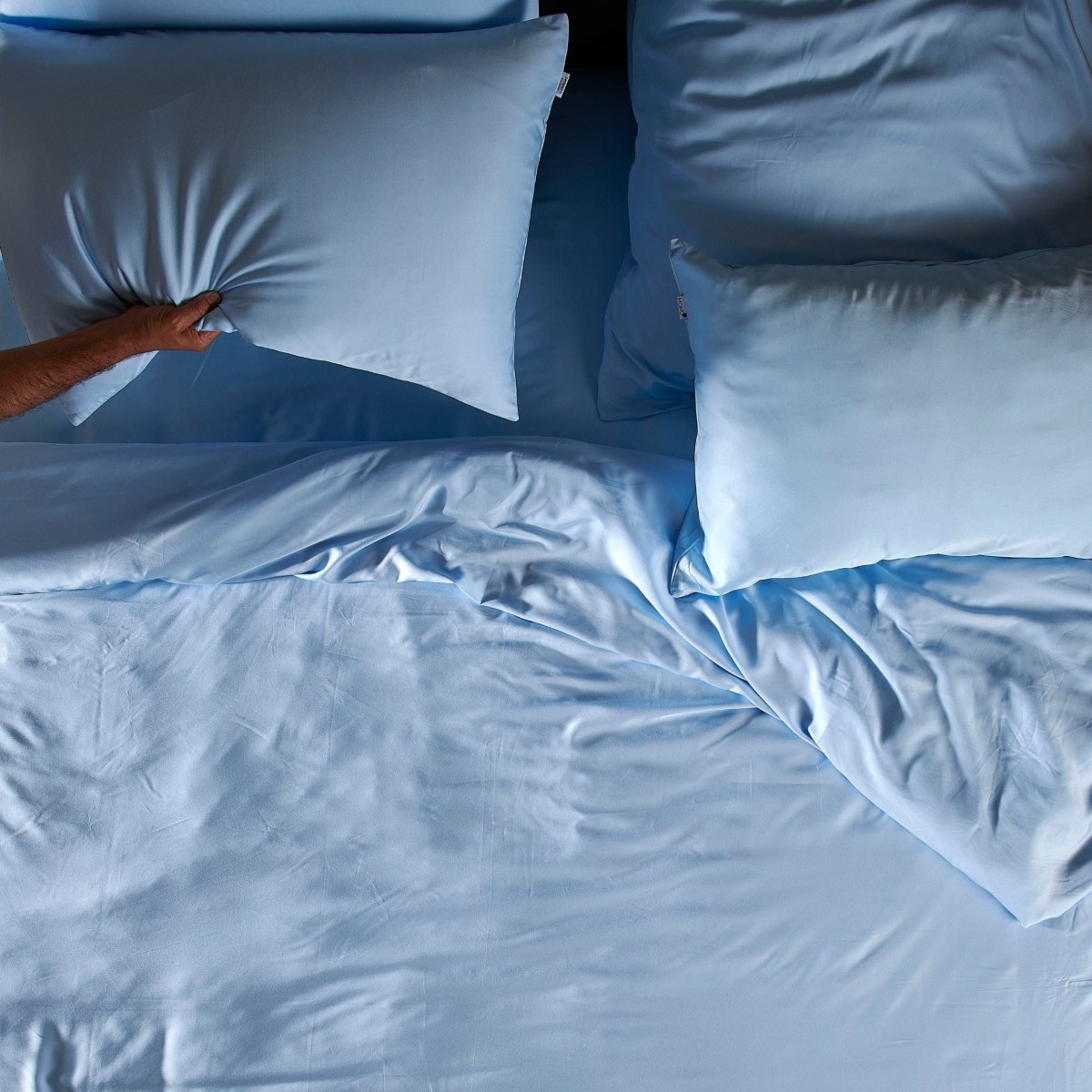 Person ordnet hellblaues Bambus-Bettwäsche-Set mit Kissen auf dem Bett an und zeigt Textur und Weichheit