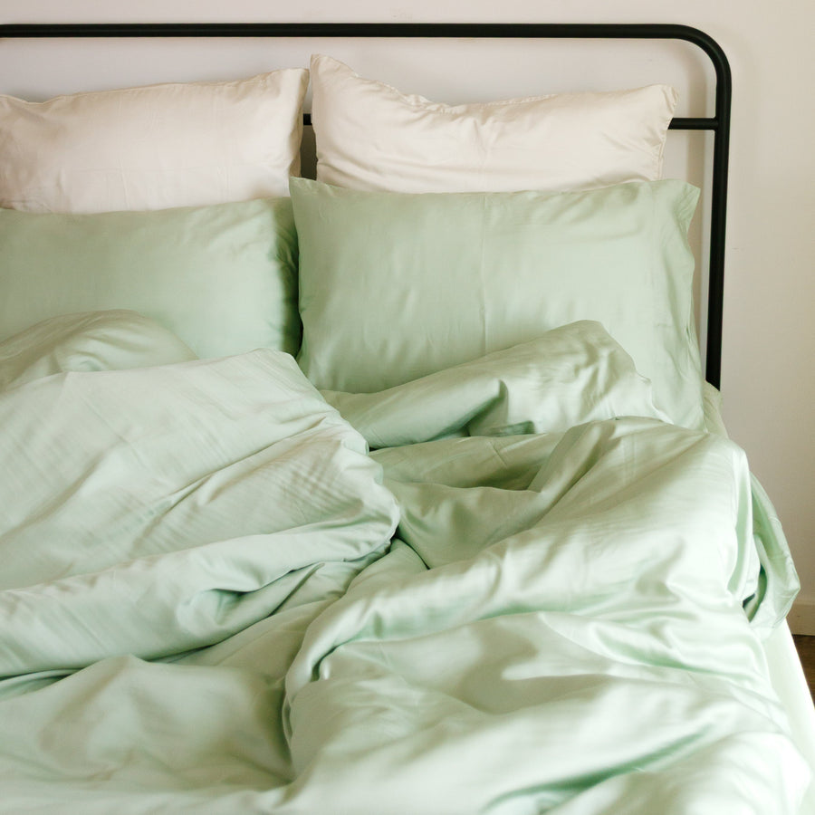 Hellgrüne und weiße Bettwäsche-Set auf Bett mit schwarzem Rahmen, Wanddeko mit Rattantellern